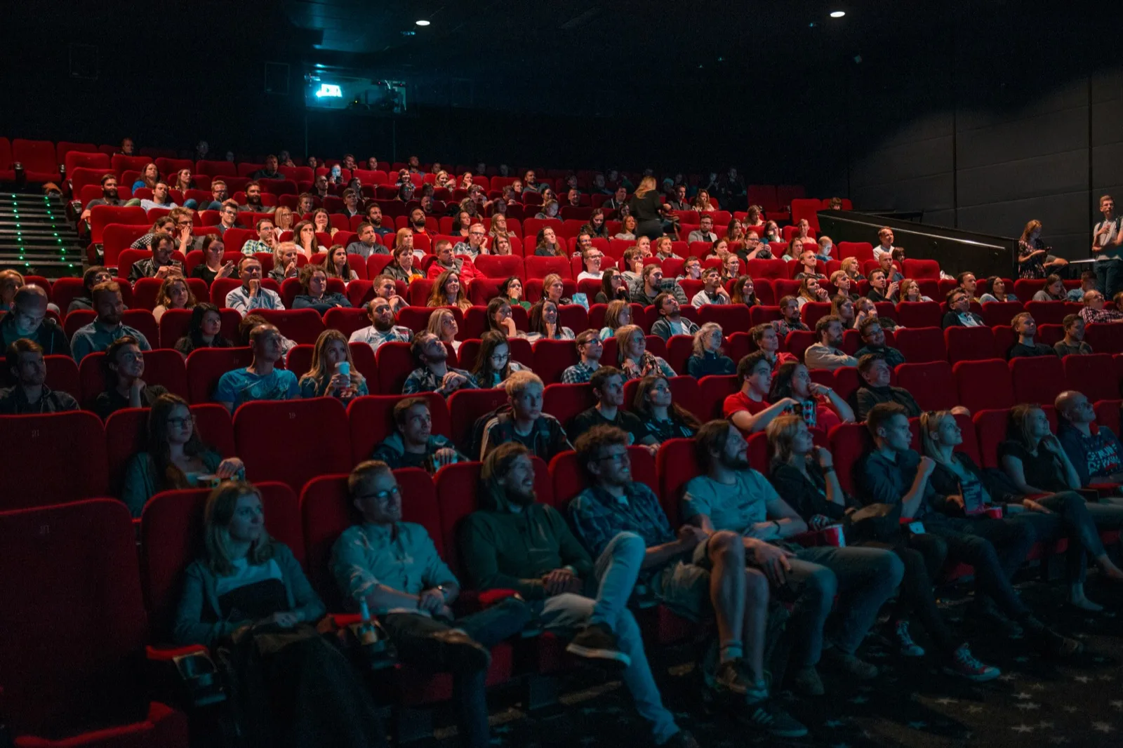 Audience seated in red theatre seats watching a performance in a darkened auditorium