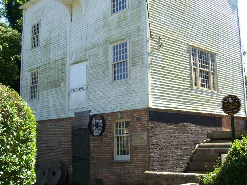 The weatherboarded Ifield Watermill building in Crawley, with its brick base and mill machinery outside